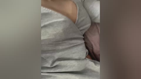 Video of a person's torso, wearing a light gray, long-sleeved shirt with a purple pillow. The image is slightly blurred and focuses on the fabric texture and the contours of the body.
