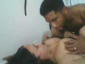 A video shows two men, one with a tan complexion and short black hair, performing oral sex on the other, who has a lighter skin tone and dark hair. They are in a bedroom with white walls.