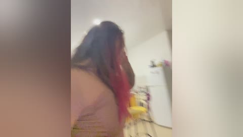 Media: A blurred video of a person with long, dark hair and a red streak, standing in a cluttered room with a white fridge and various objects.
