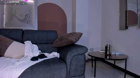 A video of a modern living room with a dark blue sofa, brown throw pillows, and a white blanket, set against a minimalist white wall.