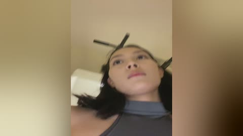 A blurred video of a young woman with short dark hair and a gray top, lying on a white chair, with metal rods attached to her head.