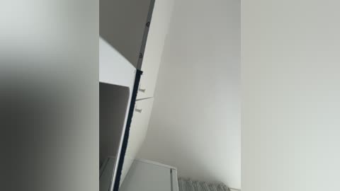 A video captures a white, circular, mirrored ceiling in an interior space. The image is minimalistic with soft lighting, revealing a corner and part of a white wall. The mirror reflects a portion of a room, hinting at modern, clean design.