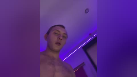 Media: A blurry video of a shirtless, light-skinned man with short hair, captured in a dimly lit room with purple LED lighting.