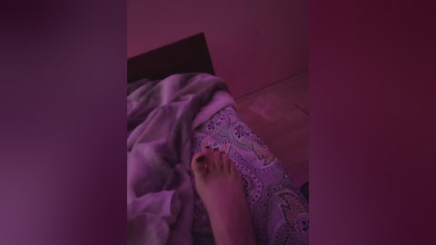 Media: A video shows a close-up of a person's hand, partially covered by a grey blanket, lying on a bed with paisley-patterned sheets. The room is dimly lit with a pinkish hue, giving a soft, intimate atmosphere.