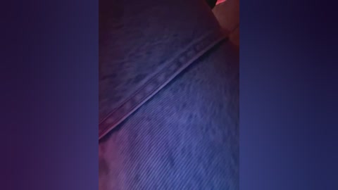 Close-up video of a person's hand with a slightly wrinkled, dark blue sleeve, featuring a subtle texture and a smooth, metallic sheen. The background is a gradient of deep purples and blues, creating a moody atmosphere.