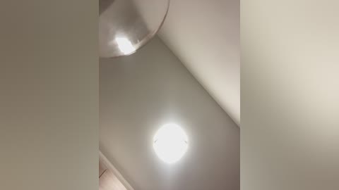 Media: Video of a ceiling with a round, bright light fixture emitting a soft glow, partially obscured by a soft, beige wall and a ceiling corner.