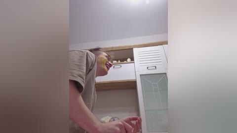 Video of a smiling young man with glasses and a yellow face mask, wearing a gray T-shirt, standing in a modern, minimalist laundry room with white lockers and shelves.