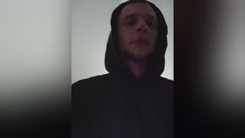 A video of a man in a dark hooded cloak, standing in a dimly lit, narrow hallway with blurry, shadowy walls, giving an ominous and mysterious atmosphere.