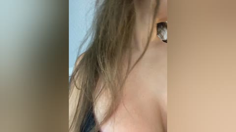Media: Video of a close-up of a woman's bare shoulder, showing a large silver hoop earring. Her long, wet hair hangs over her collarbone. The background is blurred, with beige and light blue tones.