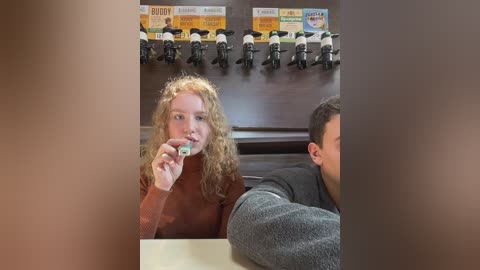 Media: Video of a woman with curly hair, wearing a brown turtleneck, holding a small object, in a fast-food restaurant with motorcycle-themed decor.