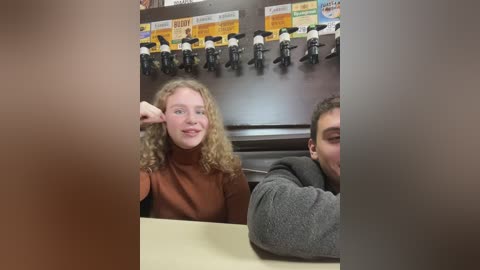 Media: A video of a young woman with curly blonde hair and a man with short dark hair, both smiling, seated at a coffee shop counter. The background features a wall-mounted coffee machine with a variety of drink options.