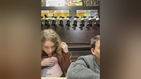 Media: Video of a woman with curly blonde hair, large breasts, and a tattoo licking a man's ear in a bar; dark wooden background with beer taps.