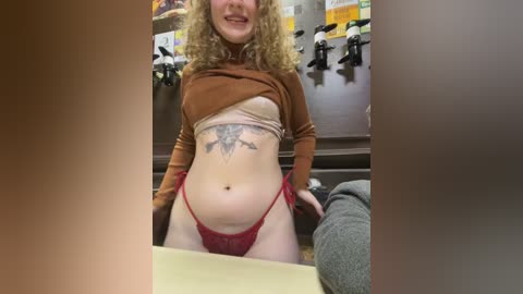Media: A video shows a plus-size woman with curly blonde hair and fair skin, wearing a brown crop top and red lace panties, standing in a dimly lit room with a tiled background and multiple faucets.