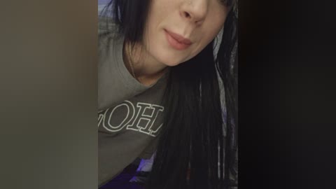 A close-up video of a young woman with long black hair, fair skin, and wearing a gray \"OOF\" t-shirt, partially cropped.