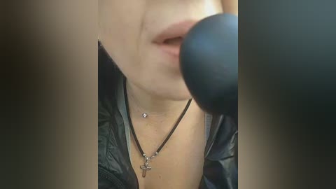 A close-up video of a woman's face, partially obscured by a black microphone, wearing a black jacket and a silver cross necklace.