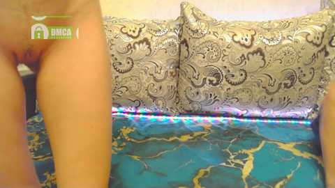 Media: Video of a woman bending over, revealing her bare genitals. She is wearing a black lace bra. Background features a patterned couch with intricate floral designs and a blue and gold marble-patterned blanket.
