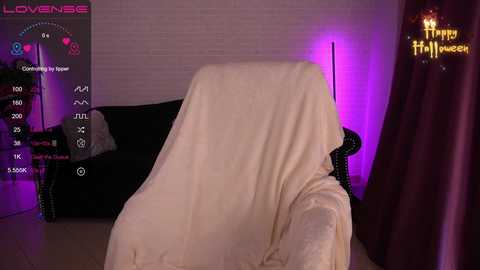A video of a dimly lit living room with a beige blanket-covered armchair, a black sofa, and a purple-lit wall, featuring a digital speedometer screen and a \"Happy Halloween\" sign.