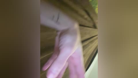A video showing a close-up of a pale hand with a tattoo, reaching through a window curtain, blurred background with green foliage.