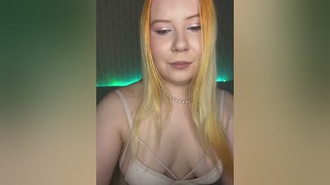 A video of a fair-skinned woman with long, vibrant orange hair, wearing a sheer, beige camisole with thin straps, against a dark, textured background with green LED lights.