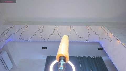 Video of a modern bedroom with a white ceiling, LED string lights, a yellow cylindrical lamp, and a round white light bulb, creating a cozy ambiance.