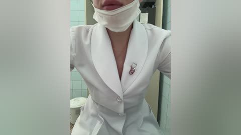 Media: A video of a woman in a white nurse's uniform with a white mask, white blouse, and white skirt. The background features tiled walls and a toilet.