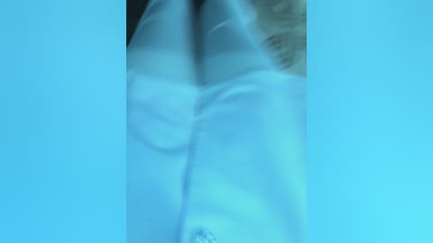 Media: Video of a person's upper body in a white lab coat, standing against a blue background. The image is slightly blurred, making it difficult to discern facial features or additional details.