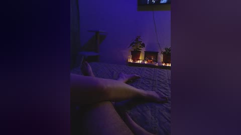 A video of a dimly-lit room with a person's legs crossed at the ankles, visible only from the thighs down. The background features a lit fireplace and potted plants. The ambiance is serene and intimate, bathed in soft, ambient lighting.