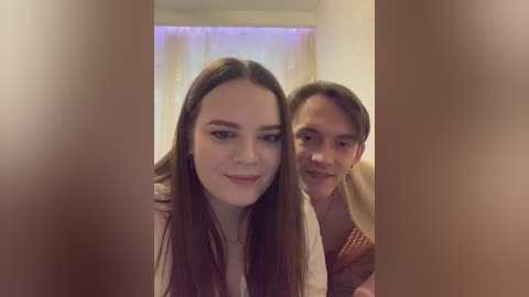 Video of a young woman with long brown hair and a fair complexion, smiling, with a young boy in the background.