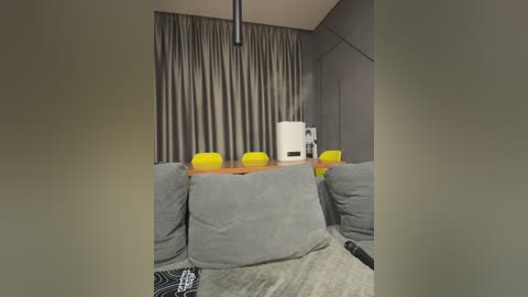 Video of a modern, minimalist cinema room with gray curtains, a wooden table, bright yellow chairs, and a white popcorn machine, featuring a cozy seating area with gray sofas and a black remote control.