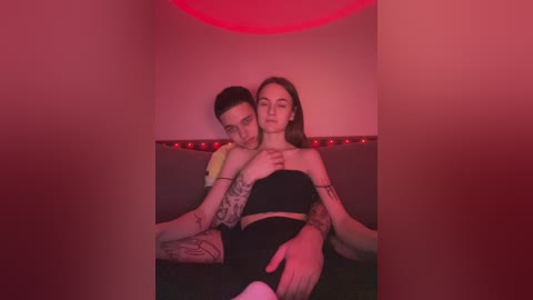 Media: A video shows a tattooed man with a lean physique embracing a slender woman with long hair, both wearing black attire, under red lighting in a dim room.