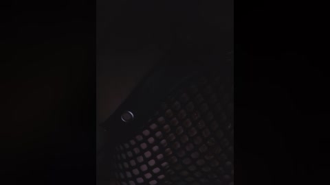 Media: A dimly lit video showing a person with fair skin and short, dark hair wearing a black mesh top. The image is grainy and heavily shadowed, creating a mysterious and somewhat creepy atmosphere.
