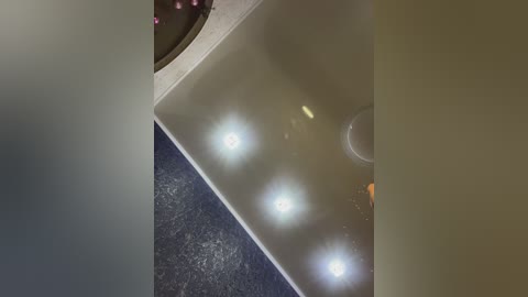 Media: A video showing a close-up of a white bathtub with four bright lights illuminating it from above, set against a dark blue tiled floor.