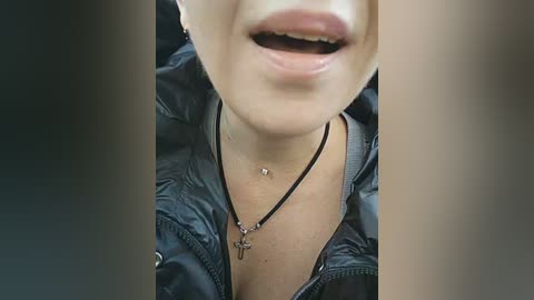 Video of a close-up of a smiling person with light skin, wearing a black leather jacket and necklace with a crucifix pendant.