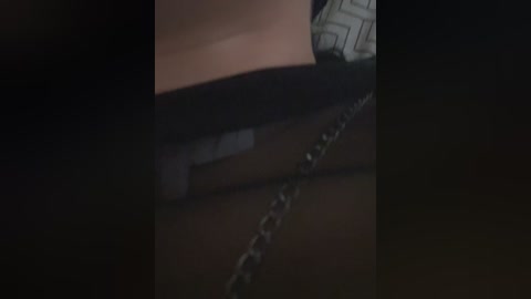 Video of a close-up, dimly lit scene featuring a person's leg shackled with a thick, heavy chain. The leg is partially visible, covered in dark clothing. The background is blurred, creating a sense of confinement and tension.
