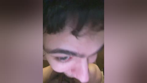 A close-up video of a young man with short dark hair, looking down, his left eyebrow slightly raised, and a pinkish hue on his nose and cheek, possibly from a slight injury or blush.