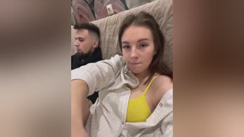 Media: A video of a young woman with long brown hair, wearing a yellow bra and unbuttoned white shirt, sitting next to a man with a beard on a train, blurred faces.