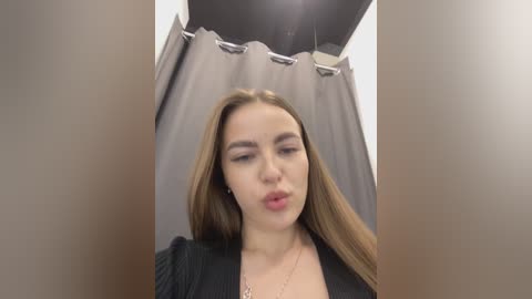Media: Video of a young woman with long brown hair, fair skin, and full lips, in a gray shower stall with a black curtain.