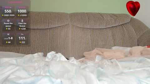 A video of a messy, beige-striped couch with a crumpled white and pastel-colored blanket, set against a light green wall.