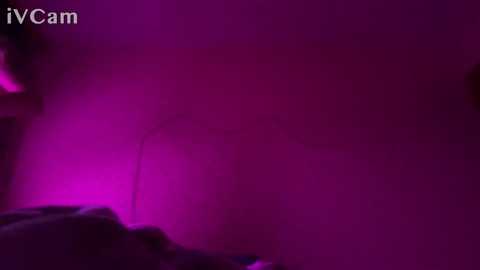 Media: A video featuring a dimly lit, magenta-colored room with blurred, indistinct figures. The background is hazy, with a faint, purple-tinted light source. The image has a \"IVCam\" watermark in the top left corner.