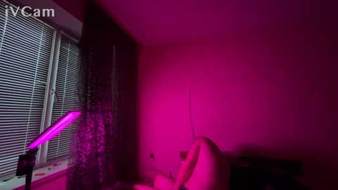 Media: A video of a dimly lit, purple-lit room with a white window and blinds. A person with fair skin and light hair is seated, partially visible.