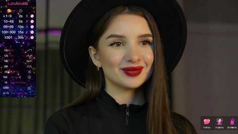 Media: Video of a young woman with long brown hair, wearing a black hat and matching outfit, smiling against a blurred background. Live streaming text overlay shows viewers and chat.