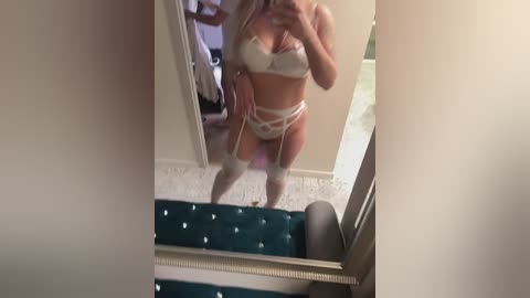 Media: A video captures a woman with fair skin and long blonde hair, wearing white lingerie with garter belts, standing in a dimly lit room with a green carpeted staircase.