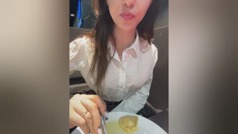 Media: A video of an East Asian woman with straight black hair, wearing a white blouse, eating a meal with a spoon, in a dimly lit restaurant.