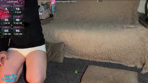 Video of a kneeling person in white underwear on a beige carpeted floor, with a video game screen displaying health bars and a character's name.