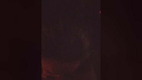 A dimly lit video shows a blurry figure with dark, messy hair and a faint red light in the background, creating a mysterious, possibly night-time scene.