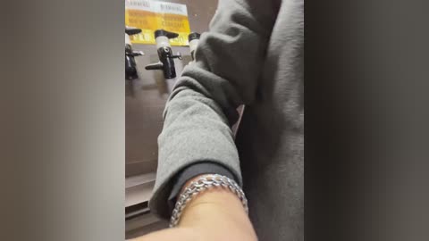 Media: Video of a person's arm in a gray jacket, holding a chain bracelet, next to a gray industrial panel with two black knobs and a yellow sticker.