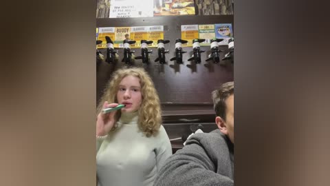 Media: Video of a blonde woman in a white turtleneck sweater brushing her teeth at a barbershop sink with a black faucet, surrounded by mounted black and white headrests.