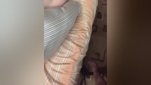 A close-up video shows a person's lower torso and legs, clad in striped pajama bottoms and a beige shirt. The background features a cluttered room with a partially visible bed and a soft, brown carpet.