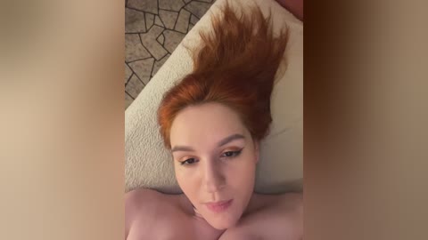 Media: A video of a topless, fair-skinned woman with red hair, lying on a beige couch with a cracked tile floor in the background.