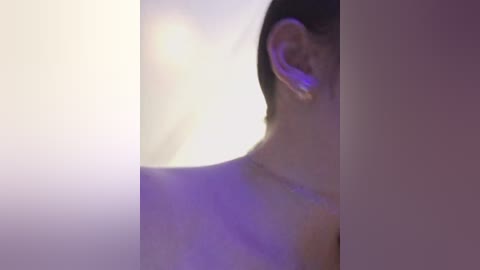 Video of a person's profile with a purple light illuminating the ear, creating a soft, dreamy effect. The background is out of focus, adding to the ethereal ambiance. The subject has short, dark hair.